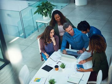 Overhead view of a diverse team of professionals reviewing documents and a laptop around a table