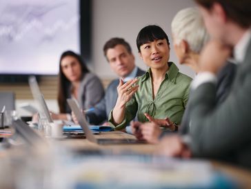 Asian woman leading a boardroom meeting with diverse colleagues around a conference table