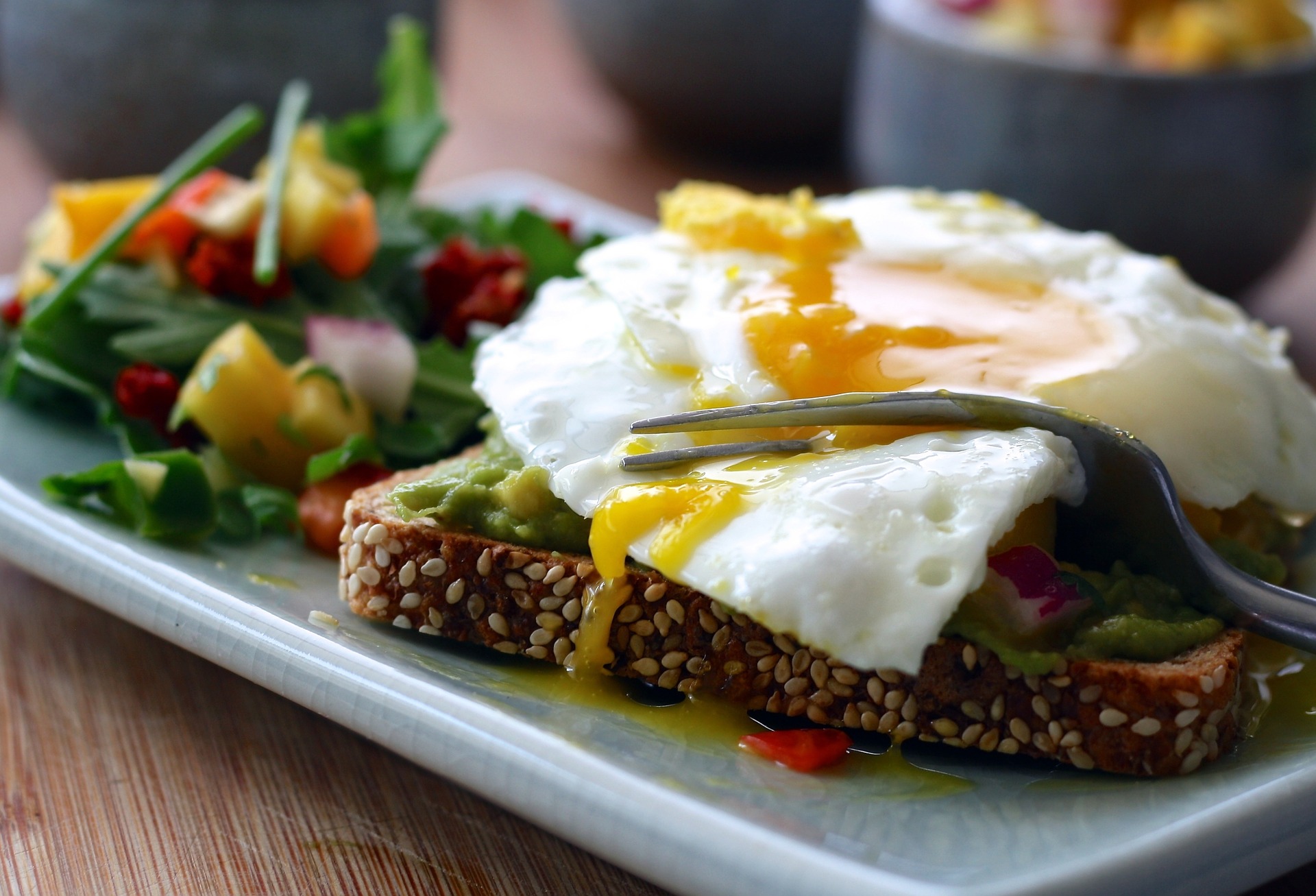 Fried egg with runny yolk on avocado toast served with a fresh salad