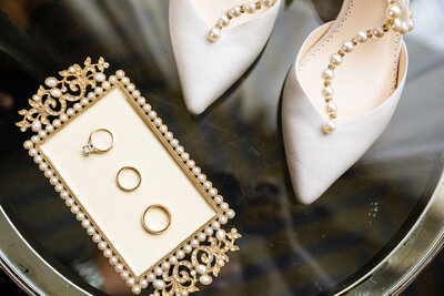 Wedding rings and pearl bridal heels on a gold ornate tray