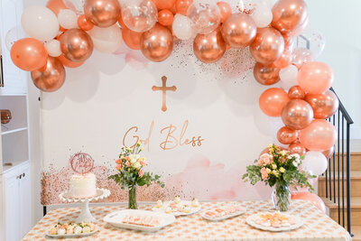 A christening dessert table with rose-gold balloon arch and floral arrangements