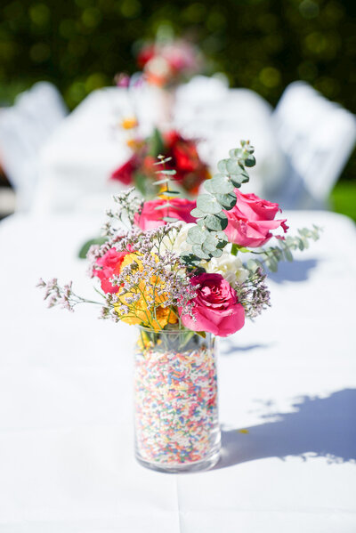Pink roses and mixed flowers in a glass vase filled with rainbow sprinkles