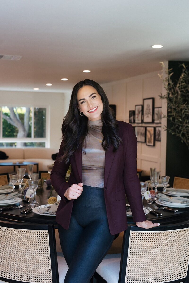 Alexandra Modon in a burgundy blazer, leaning on an elegantly set dining table