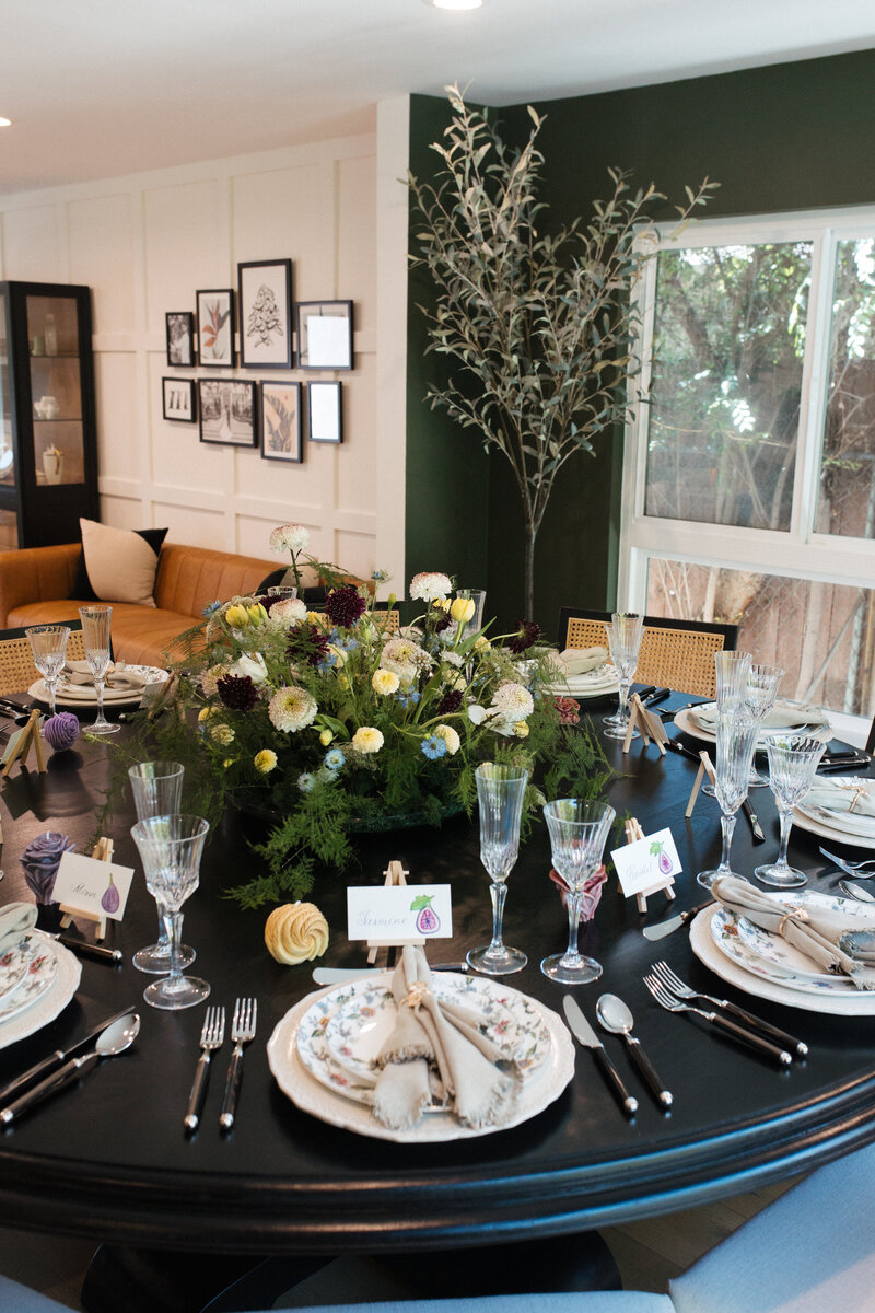 An elegantly set round dining table with floral centerpiece, crystal glasses and place cards