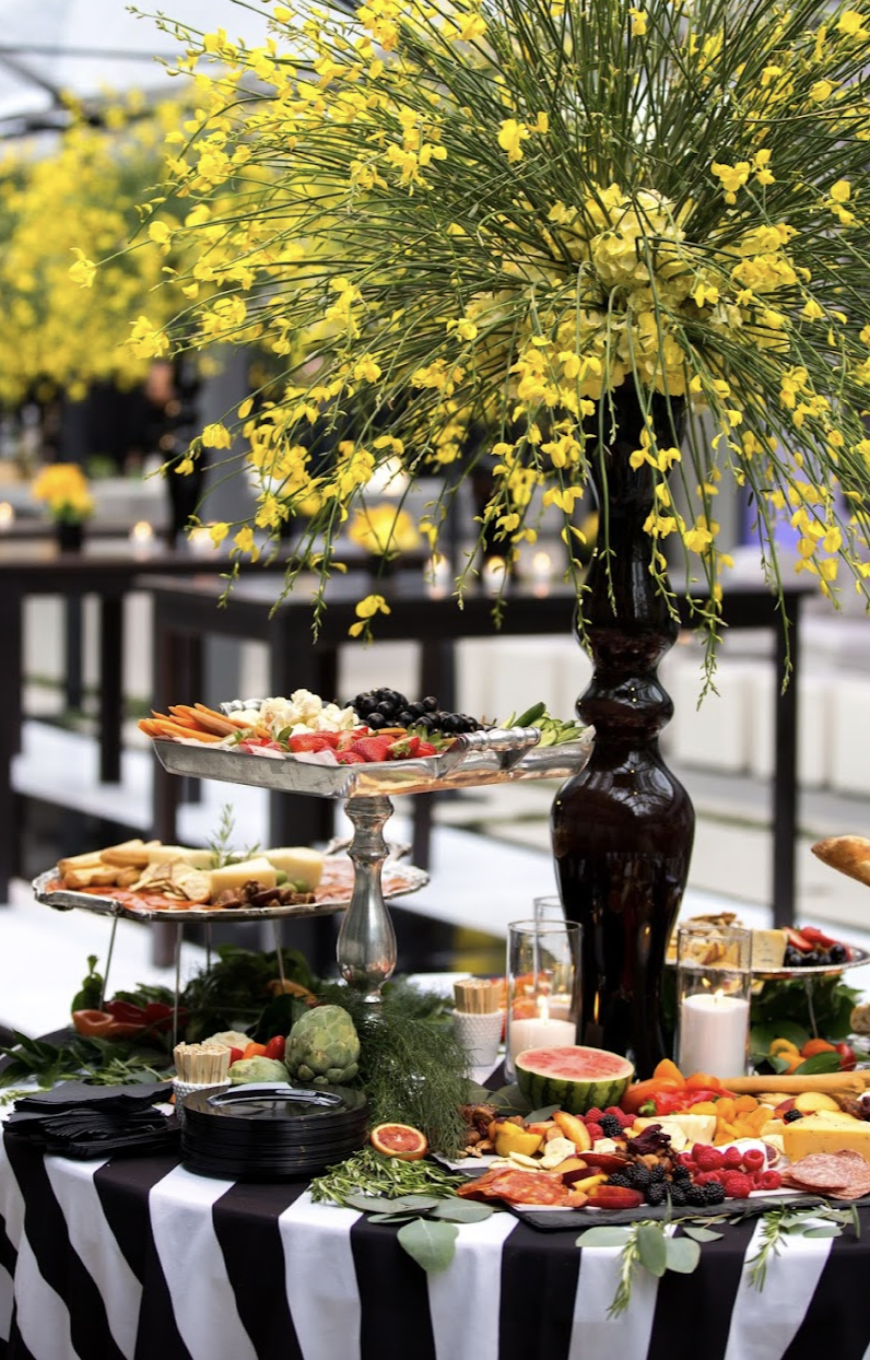 Catering display table with tall yellow orchid arrangement and tiered platters