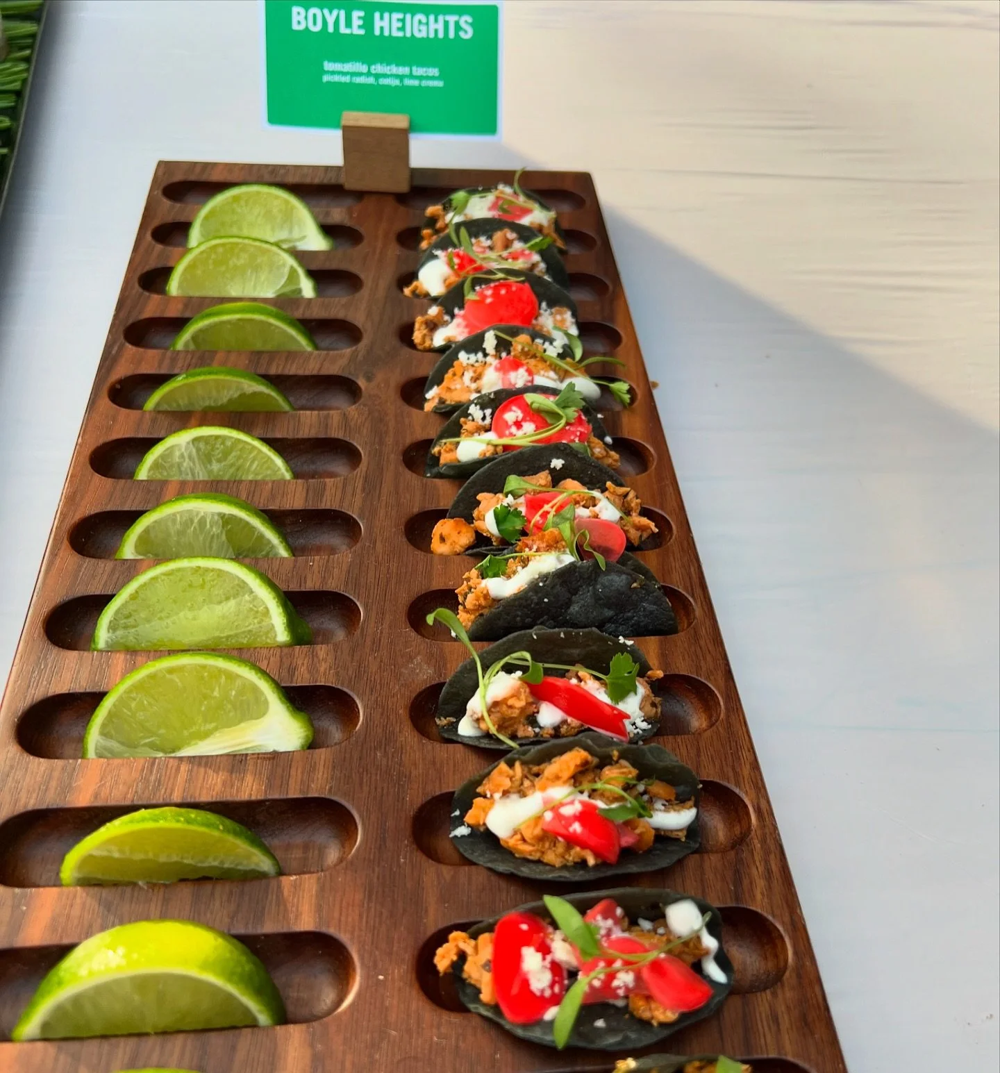 Black corn mini tacos labeled Boyle Heights on a wooden holder
