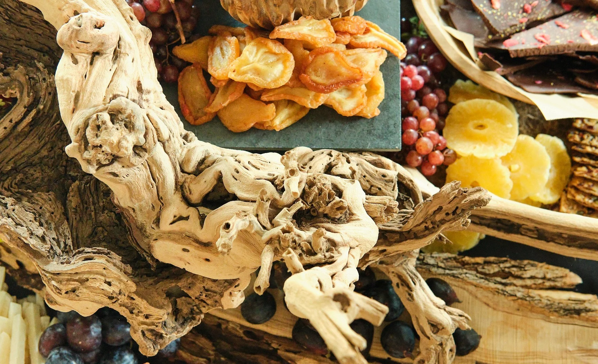 Driftwood centerpiece surrounded by grapes, dried fruit and chocolate on a grazing board