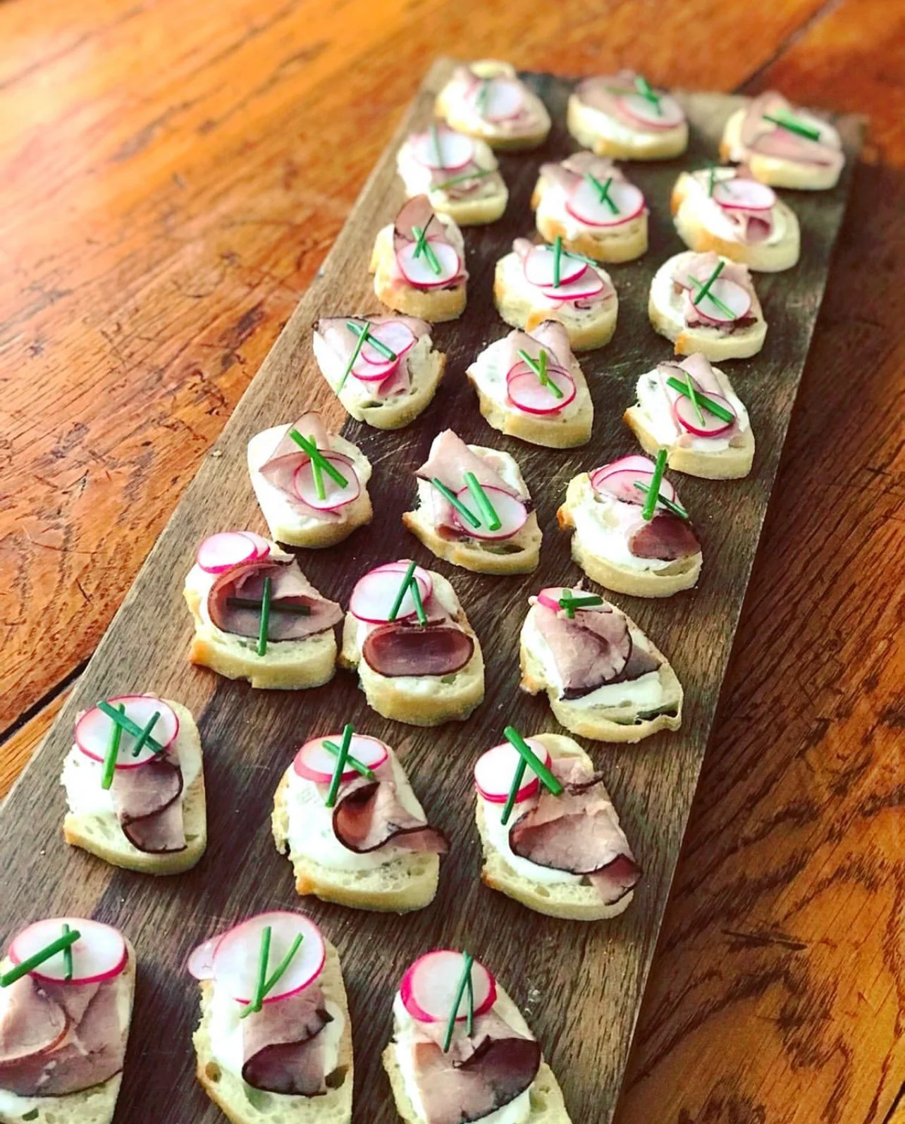 Crostini board topped with sliced meat, radish and chives