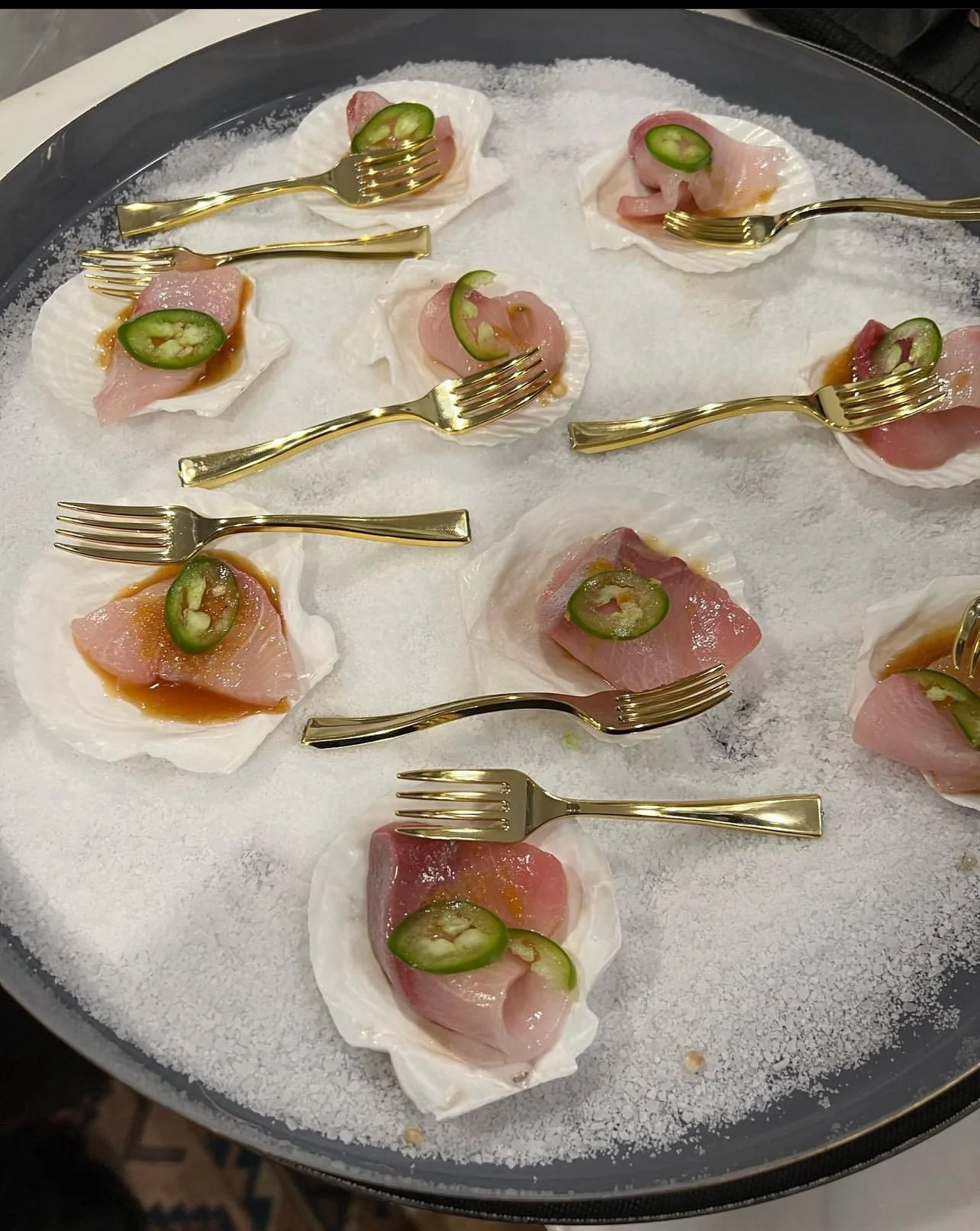 Tuna crudo on scallop shells with gold forks on ice