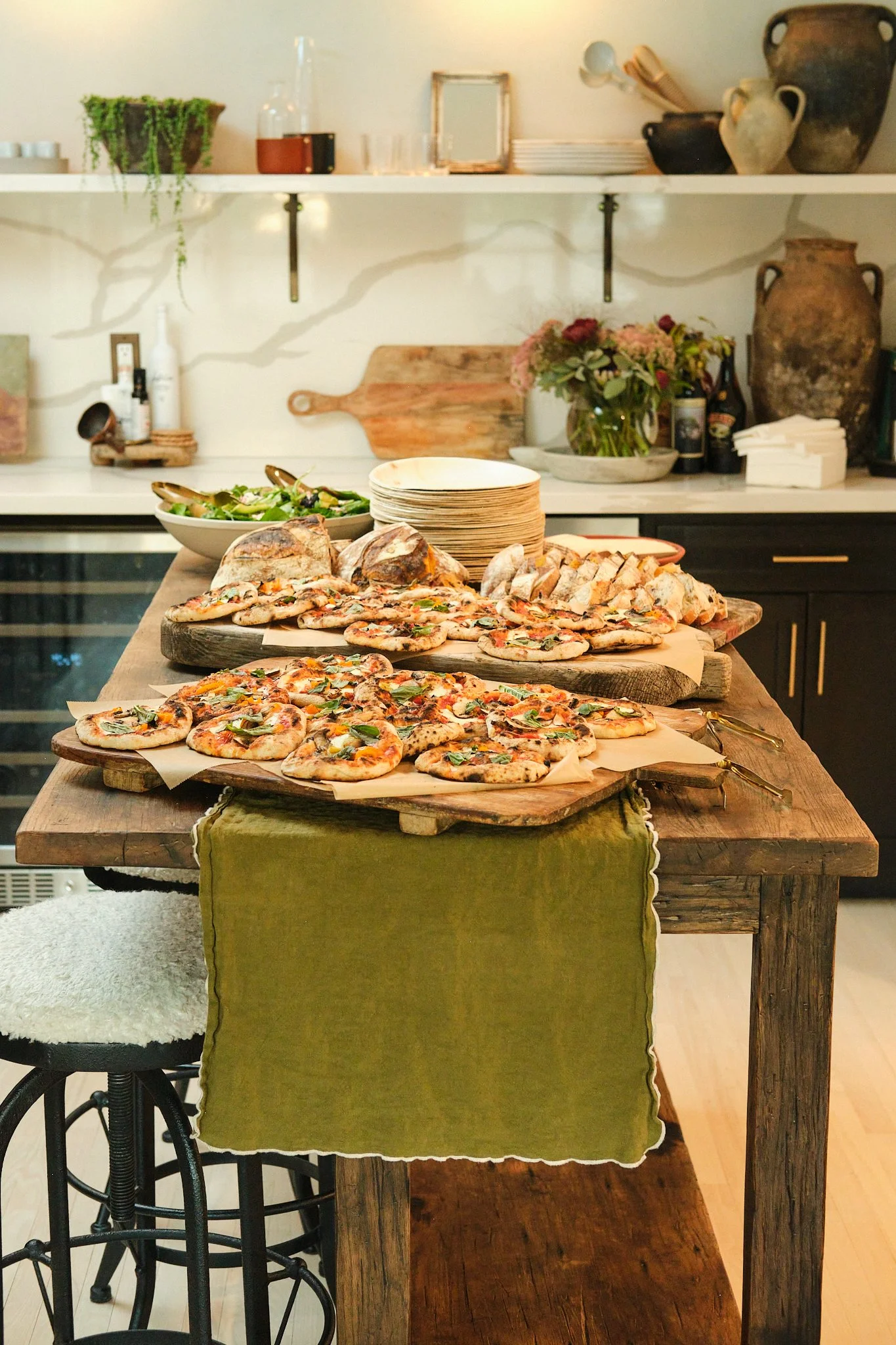 Rustic kitchen island loaded with flatbread pizzas and bread