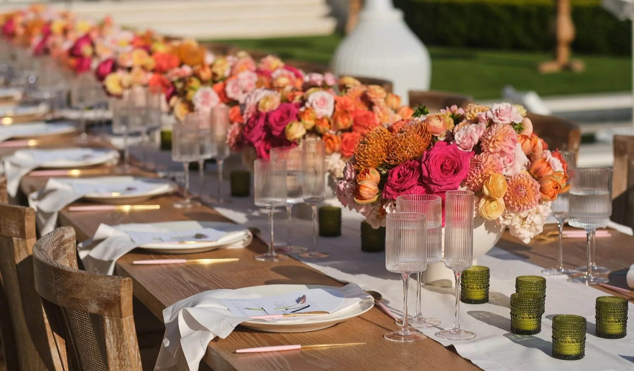 Long outdoor banquet table with vibrant pink and coral floral centerpieces