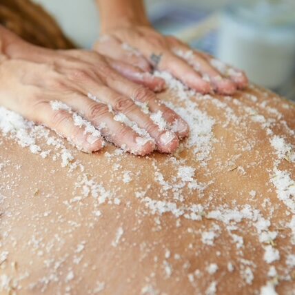 Hands applying salt scrub exfoliation to a client's back