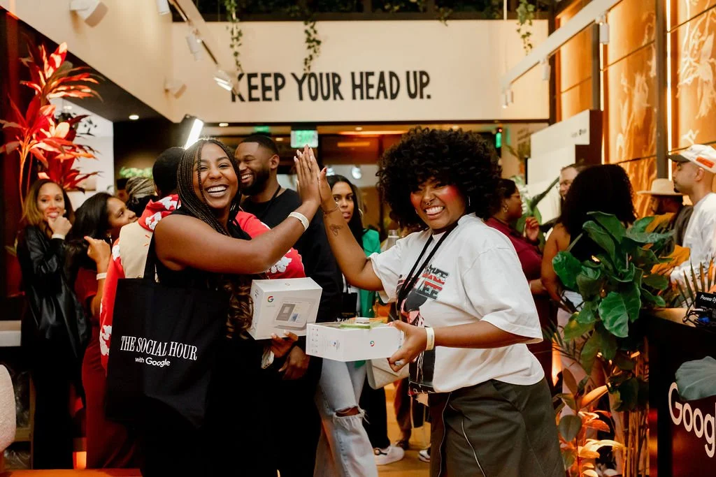 Two women high-fiving and holding Google product boxes at The Social Hour with Google