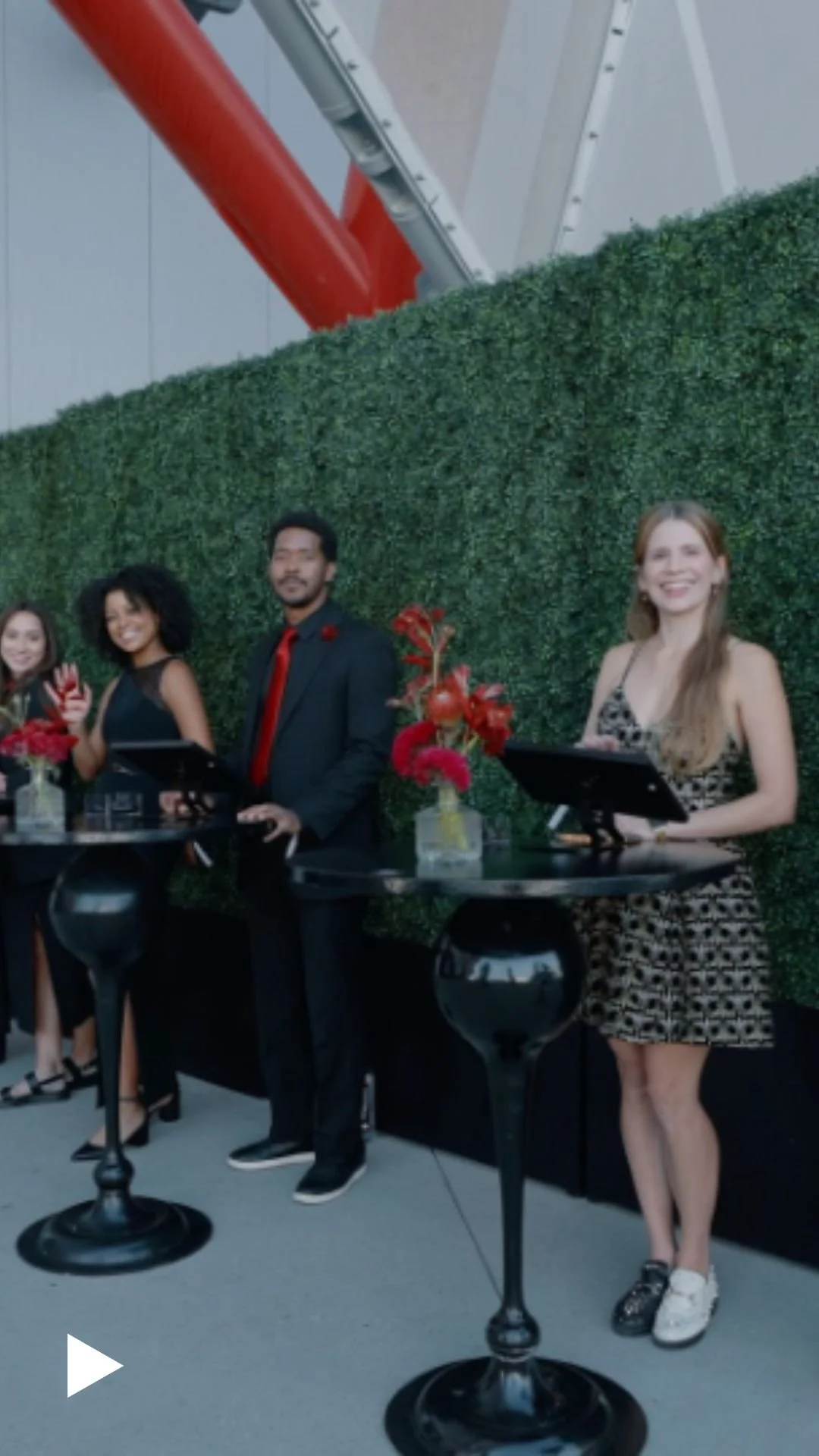 Event staff at high-top tables with a green hedge wall backdrop