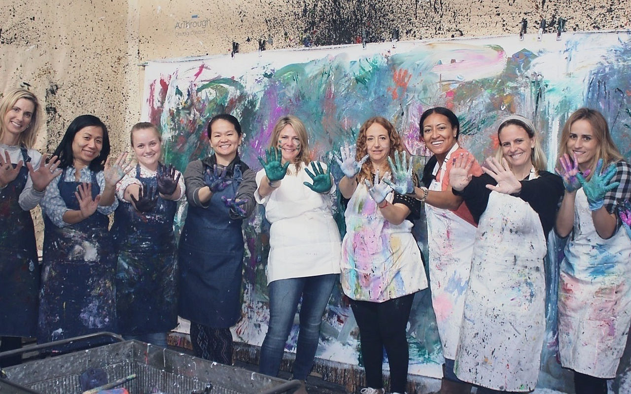 Nine women with paint-covered hands at an art workshop