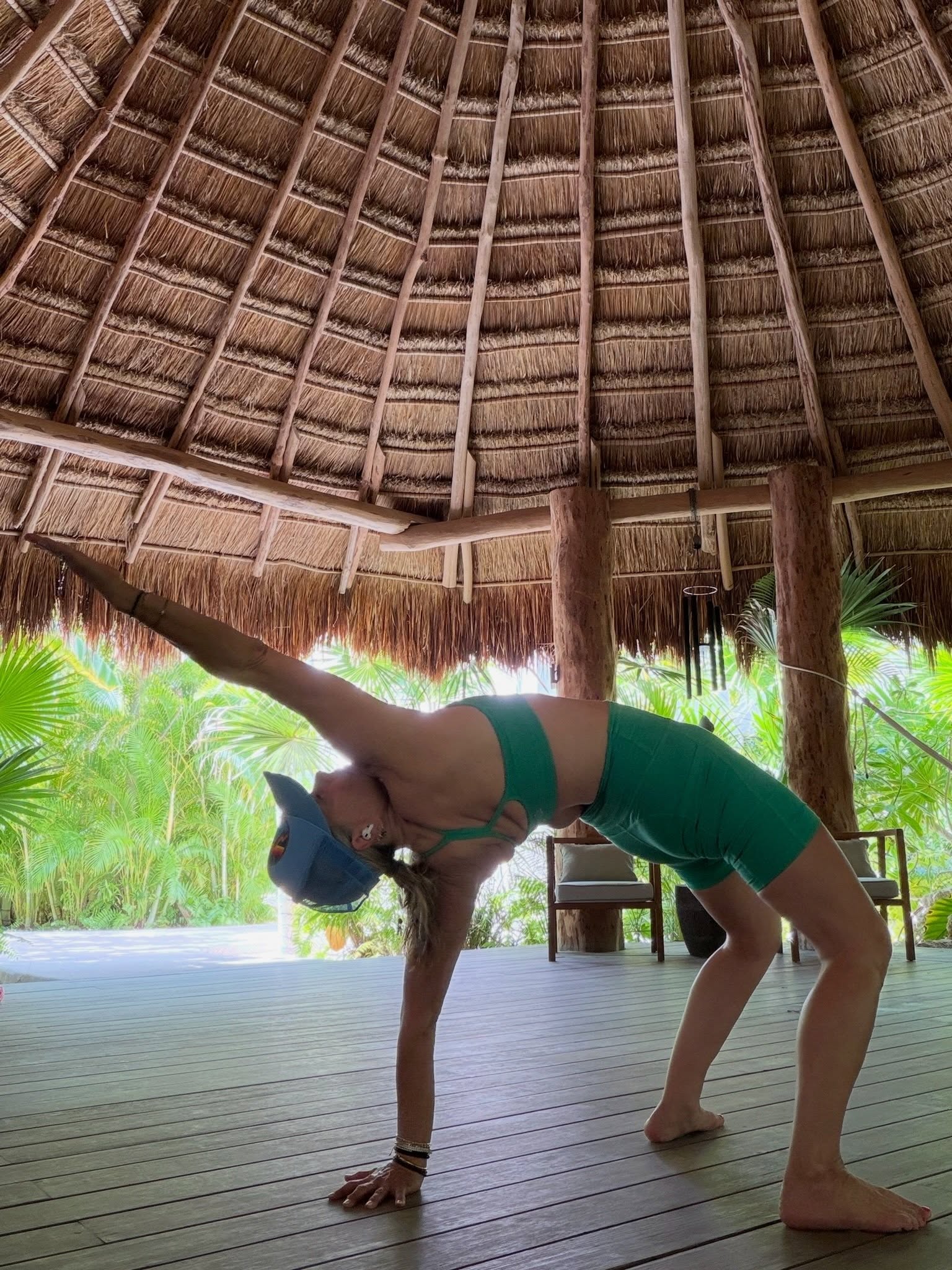 Woman in green athletic wear doing a yoga pose under a palapa