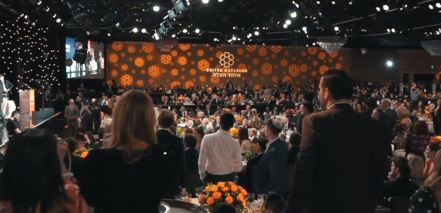 Large formal gala with hundreds of guests and an orange United Hatzalah stage backdrop