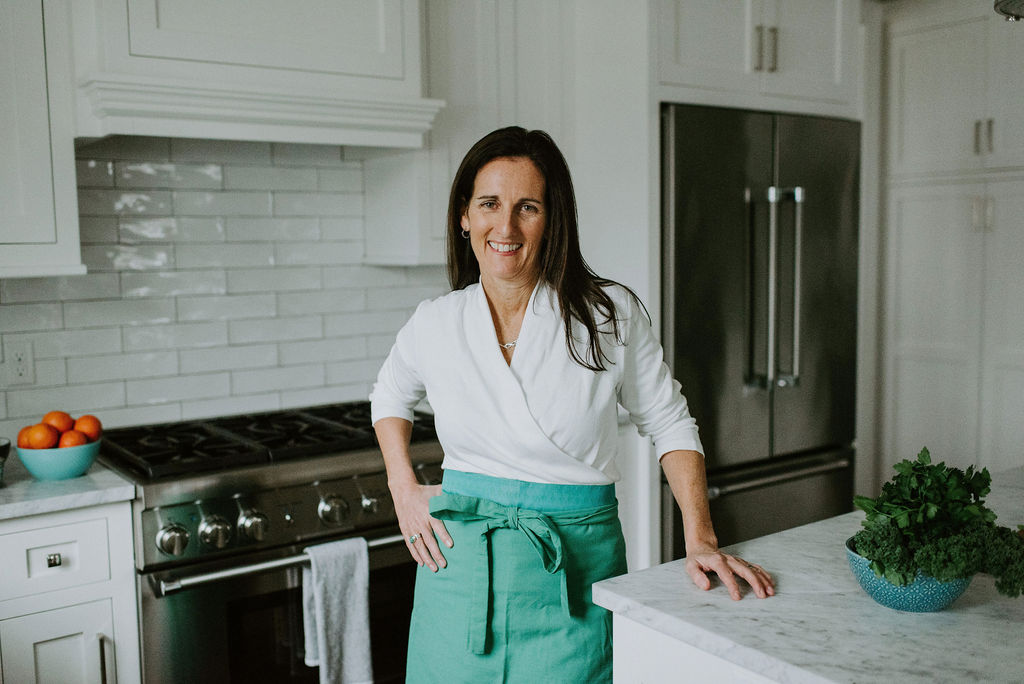 Heather Carey smiling in her bright kitchen, leaning on a marble counter