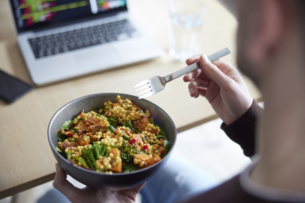 Person at a desk holding a grain and vegetable bowl with a fork