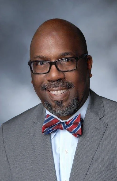 Dr. Reginald Tucker-Seeley, a man with glasses and a bow tie, smiling.