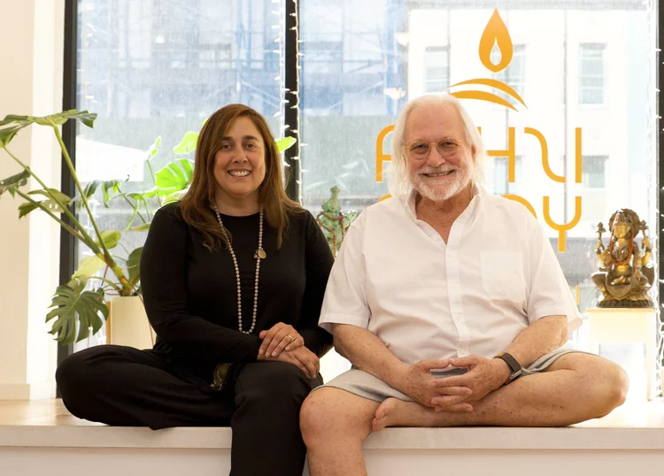 Mona Anand and Alan Finger seated before the ISHTA Yoga logo window
