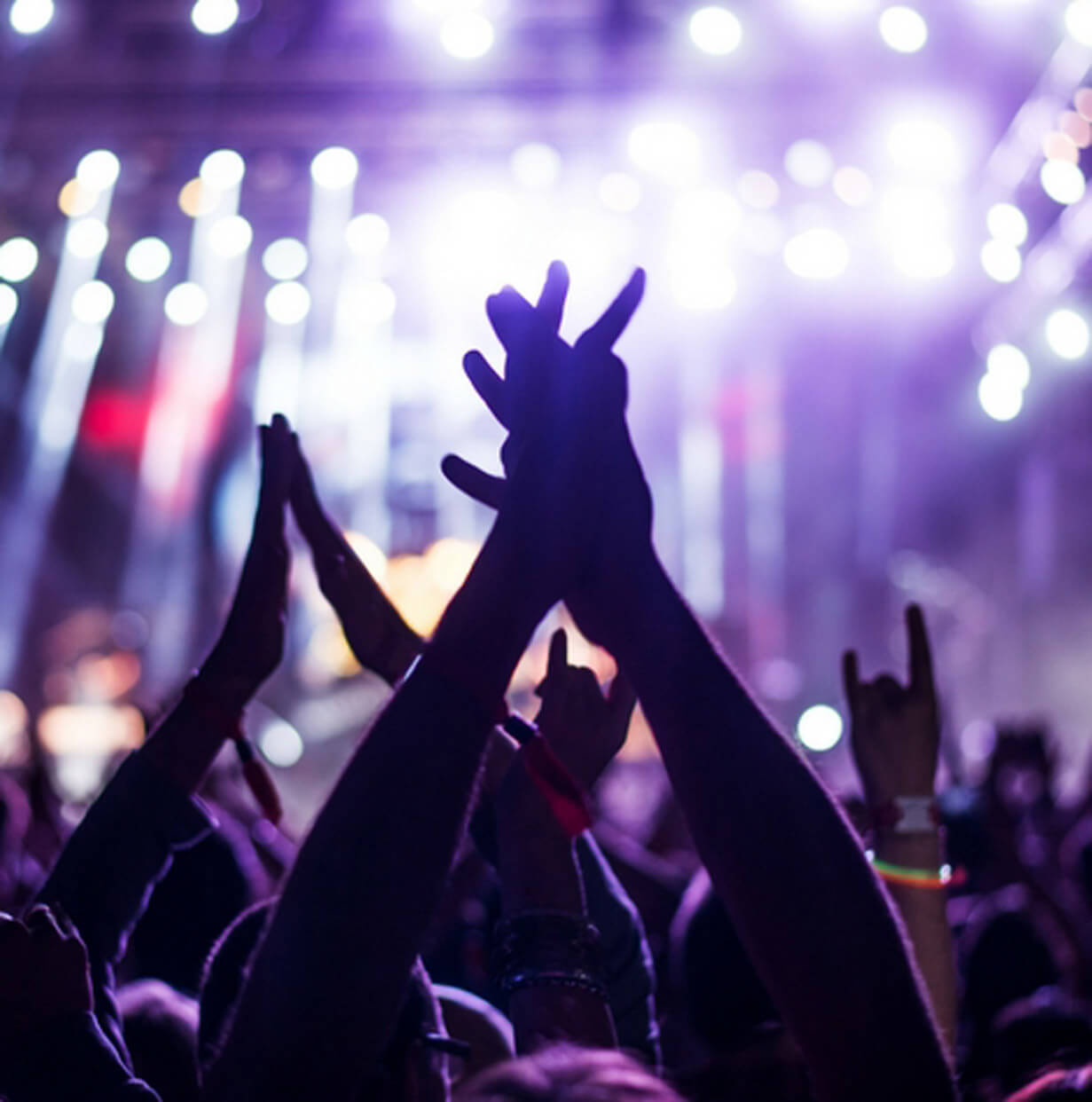 Concert crowd with hands raised, silhouetted against purple stage lights