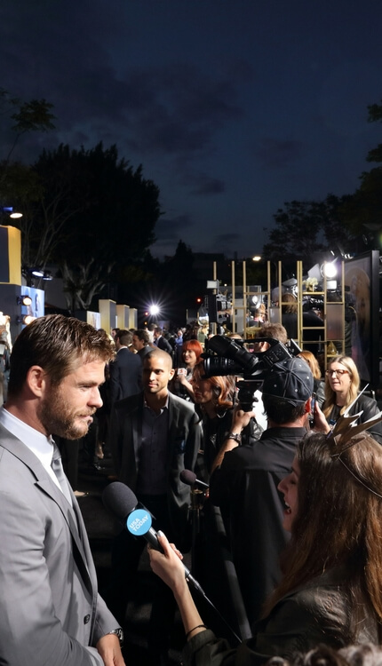 Male celebrity being interviewed by press on red carpet at night premiere