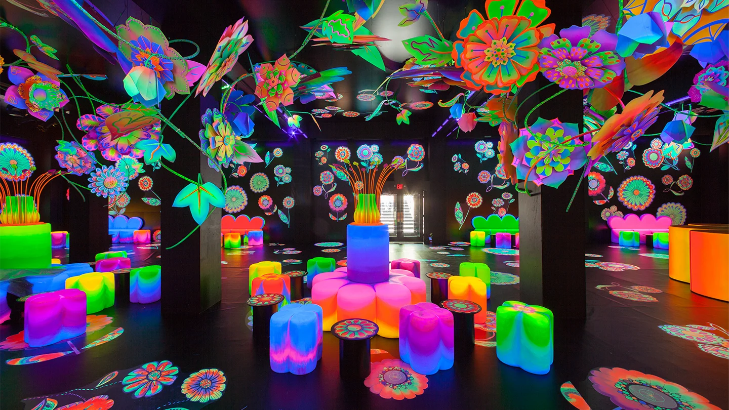 Neon blacklight floral immersive event installation with glowing furniture and giant paper flowers