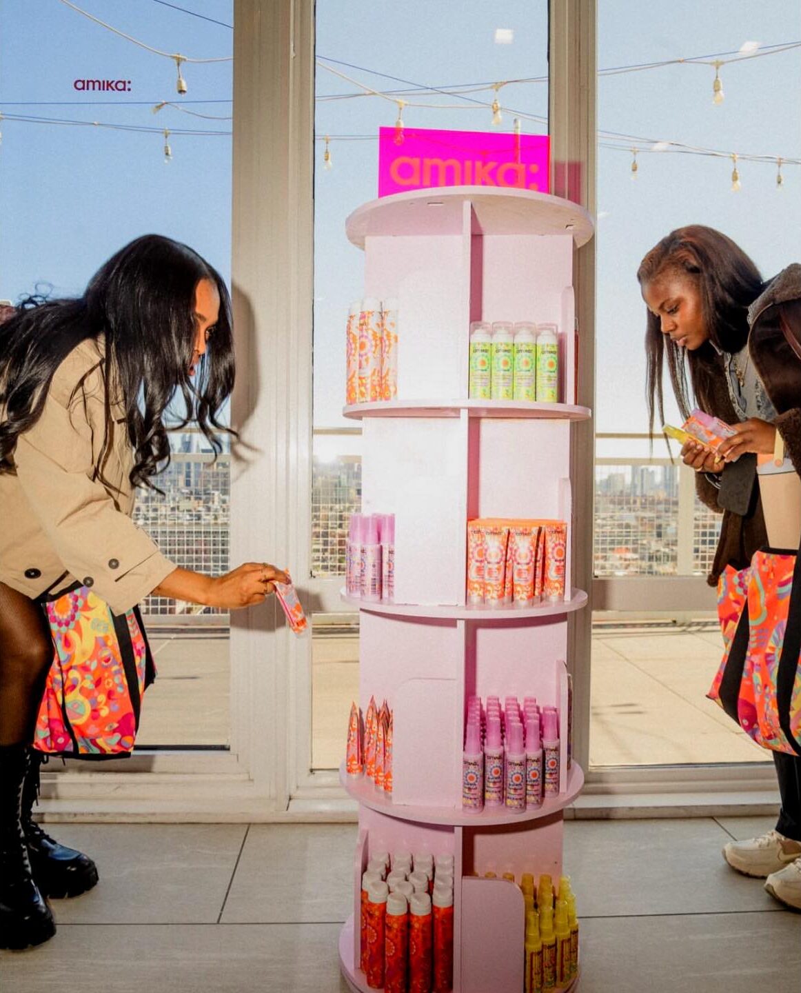 Two women examining amika hair care products at a pink revolving rooftop display