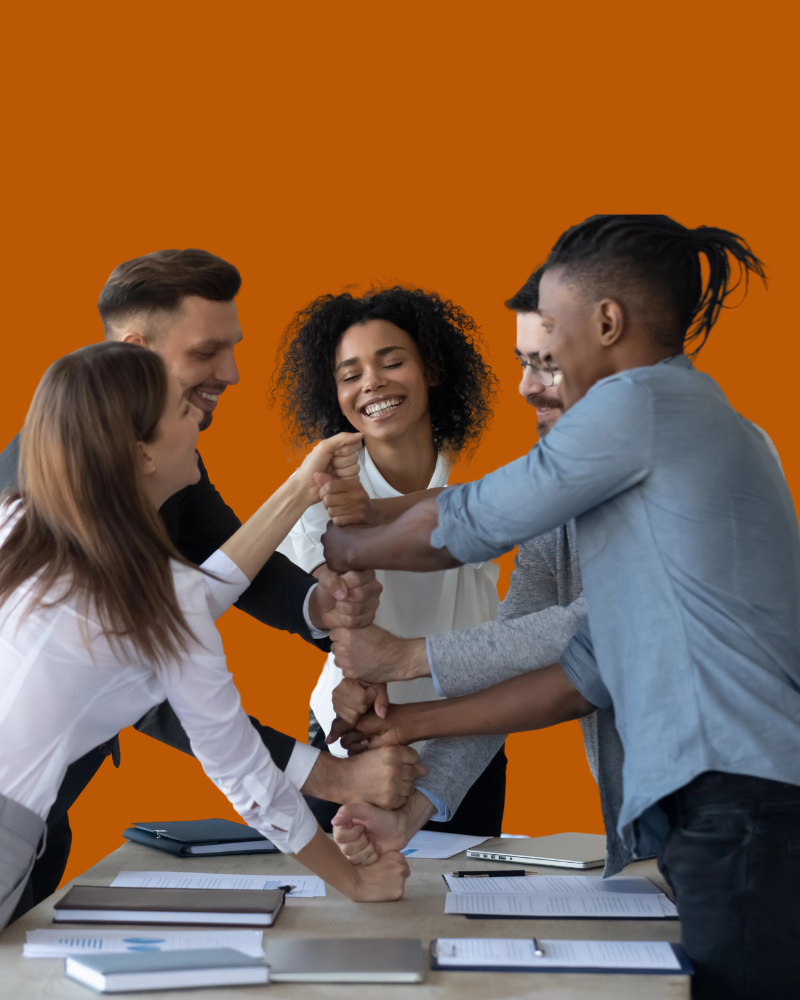 Five diverse coworkers laughing and sharing a group fist-bump over a conference table