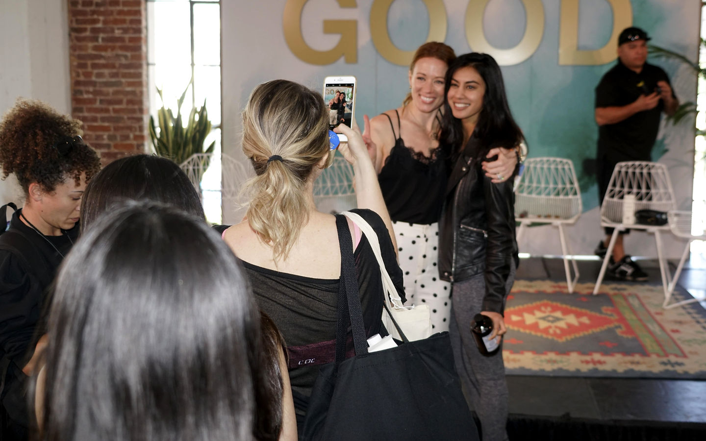Women posing at an event with a gold 'GOOD' backdrop
