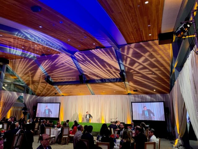 Conference in a wood-paneled venue with blue ceiling lighting