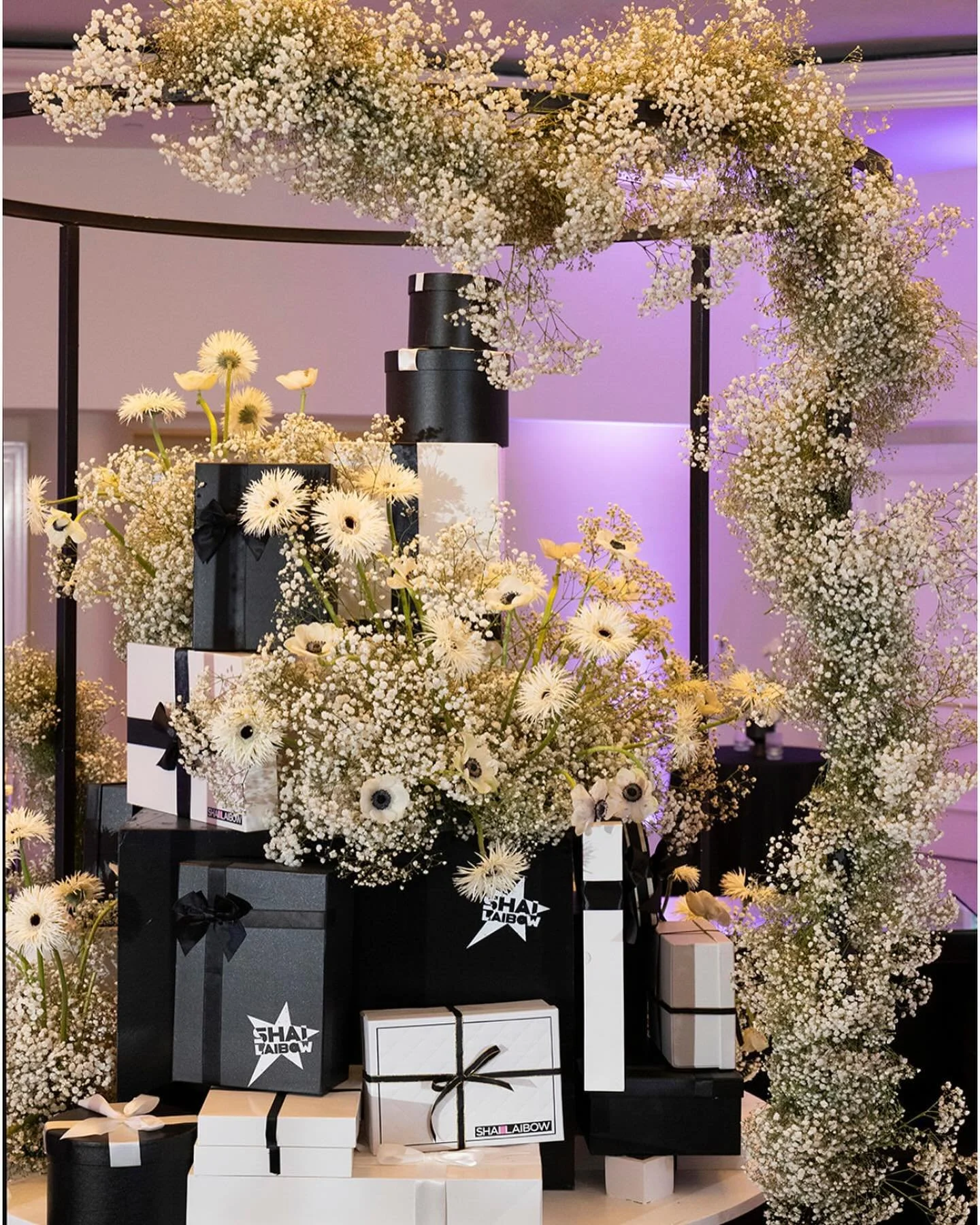 Shai Laibow gift table — branded boxes under a floral arch