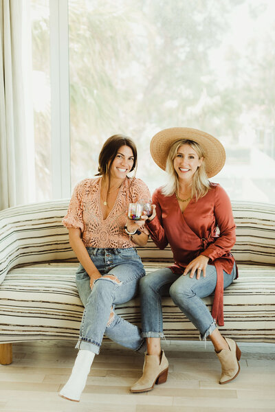Two women of LB Events seated on a striped sofa holding wine glasses