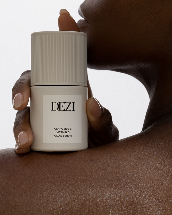 Dezi Skin Claro Que C Vitamin C Glow Serum bottle held against dark skin shoulder.