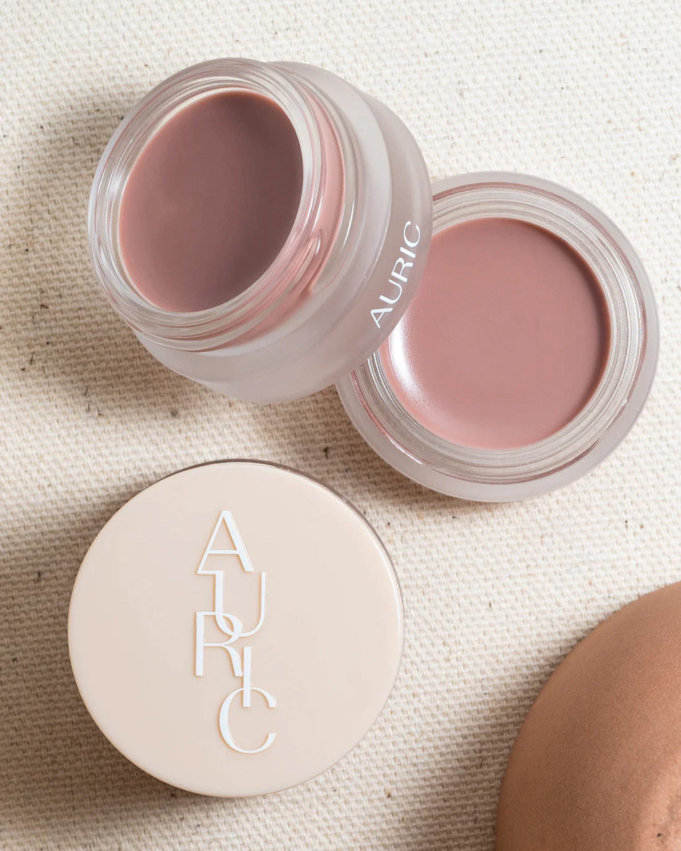 Auric Plush Ritual lip mask jar open with its lid displaying the AURIC logo, overhead flat-lay on a linen background.