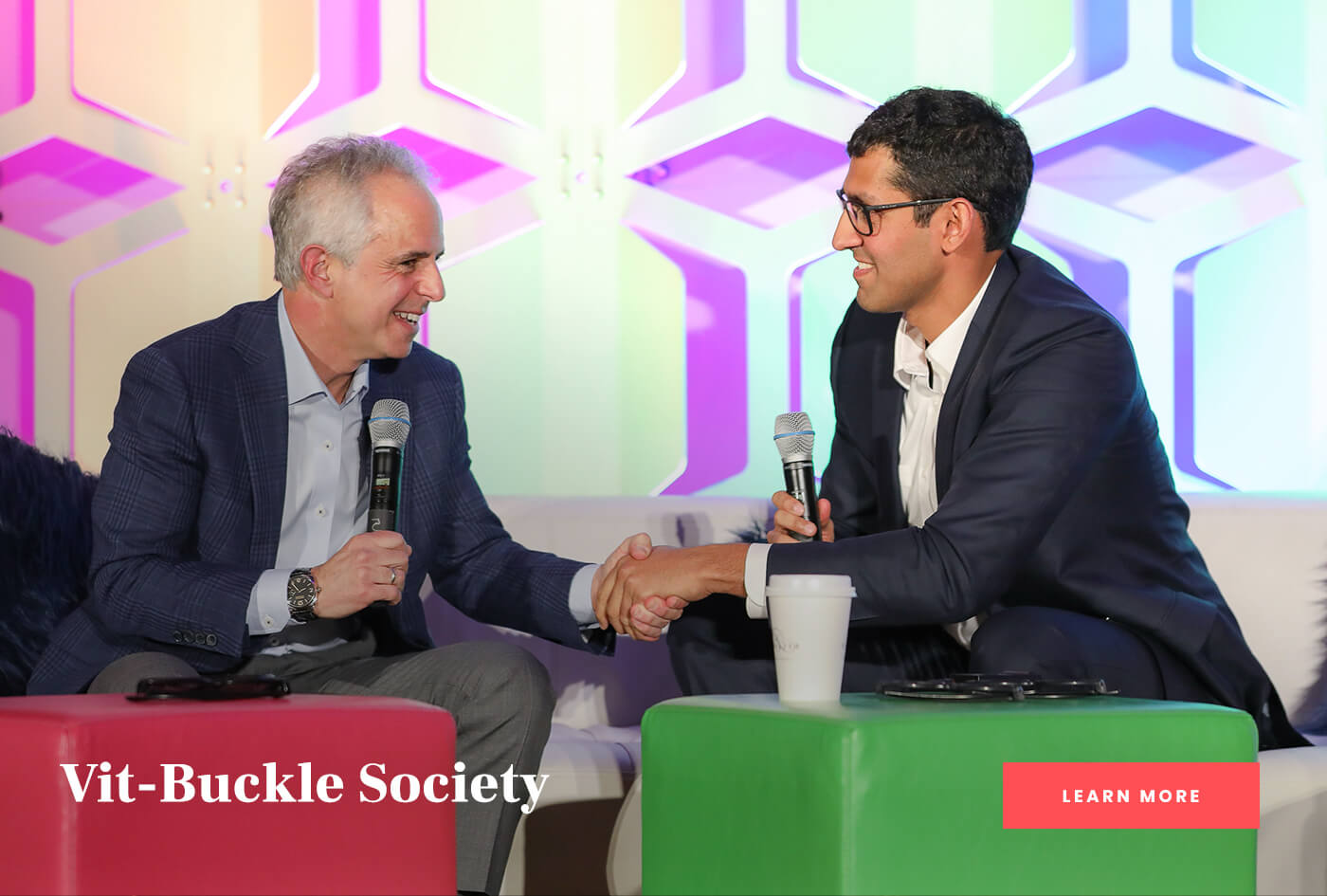Two speakers shaking hands on stage at the Vit-Buckle Society