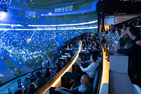 Luxury arena suite packed with guests under blue stage lighting