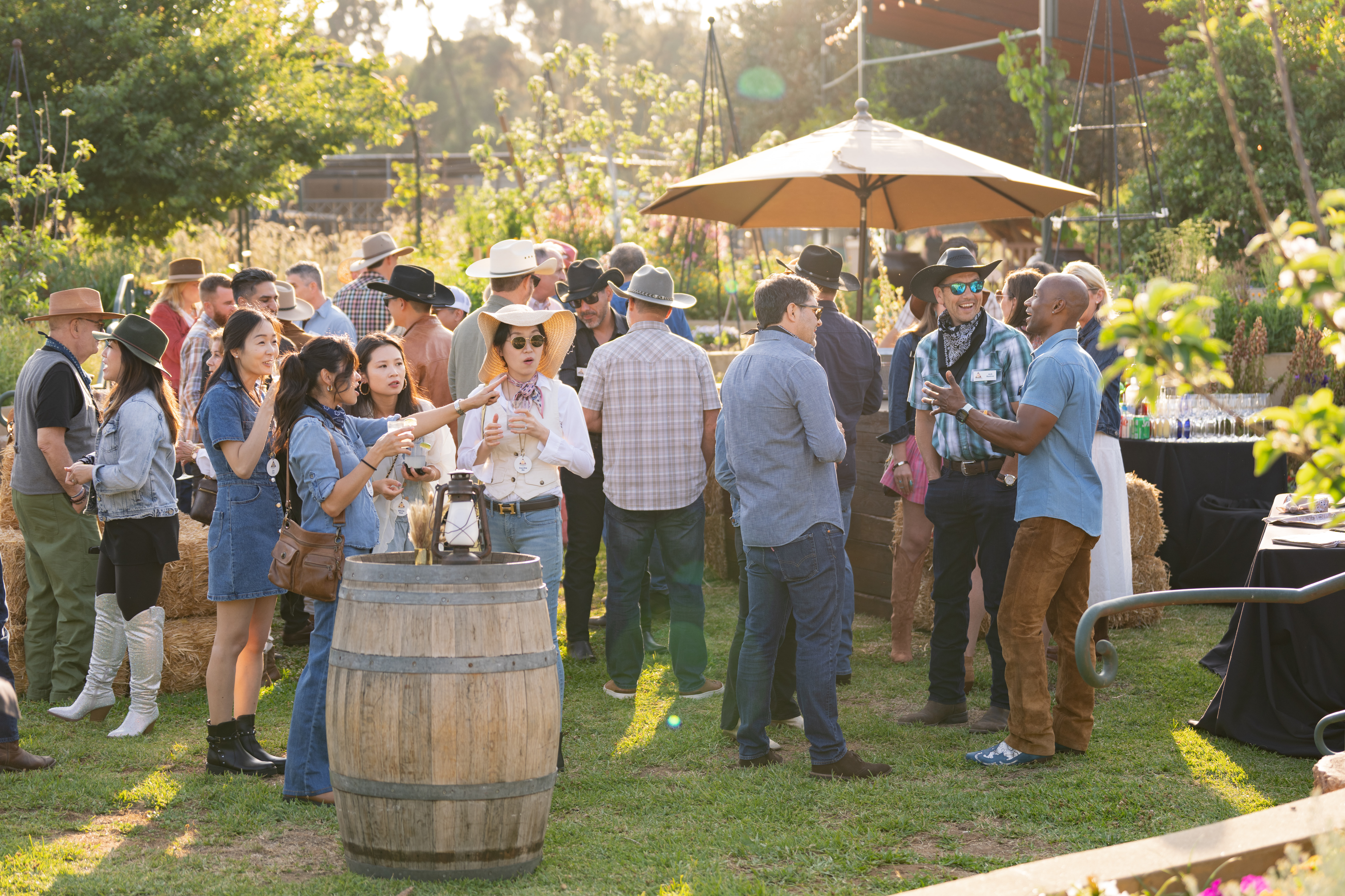 Outdoor western-themed corporate event with guests in cowboy hats among wine barrels at golden hour