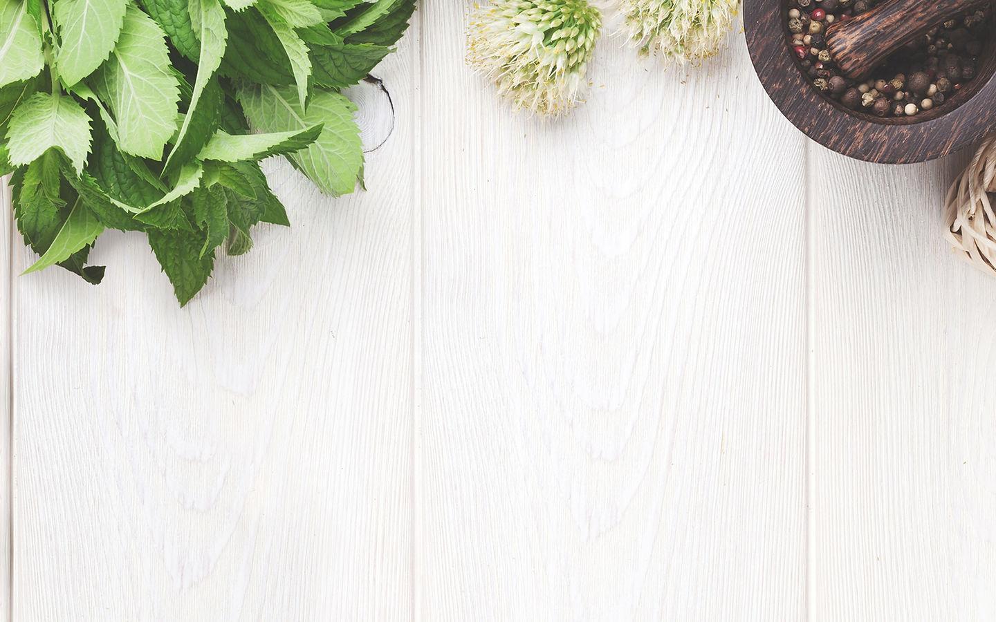 Fresh mint leaves, white flowers, and a mortar and pestle on a white wood surface