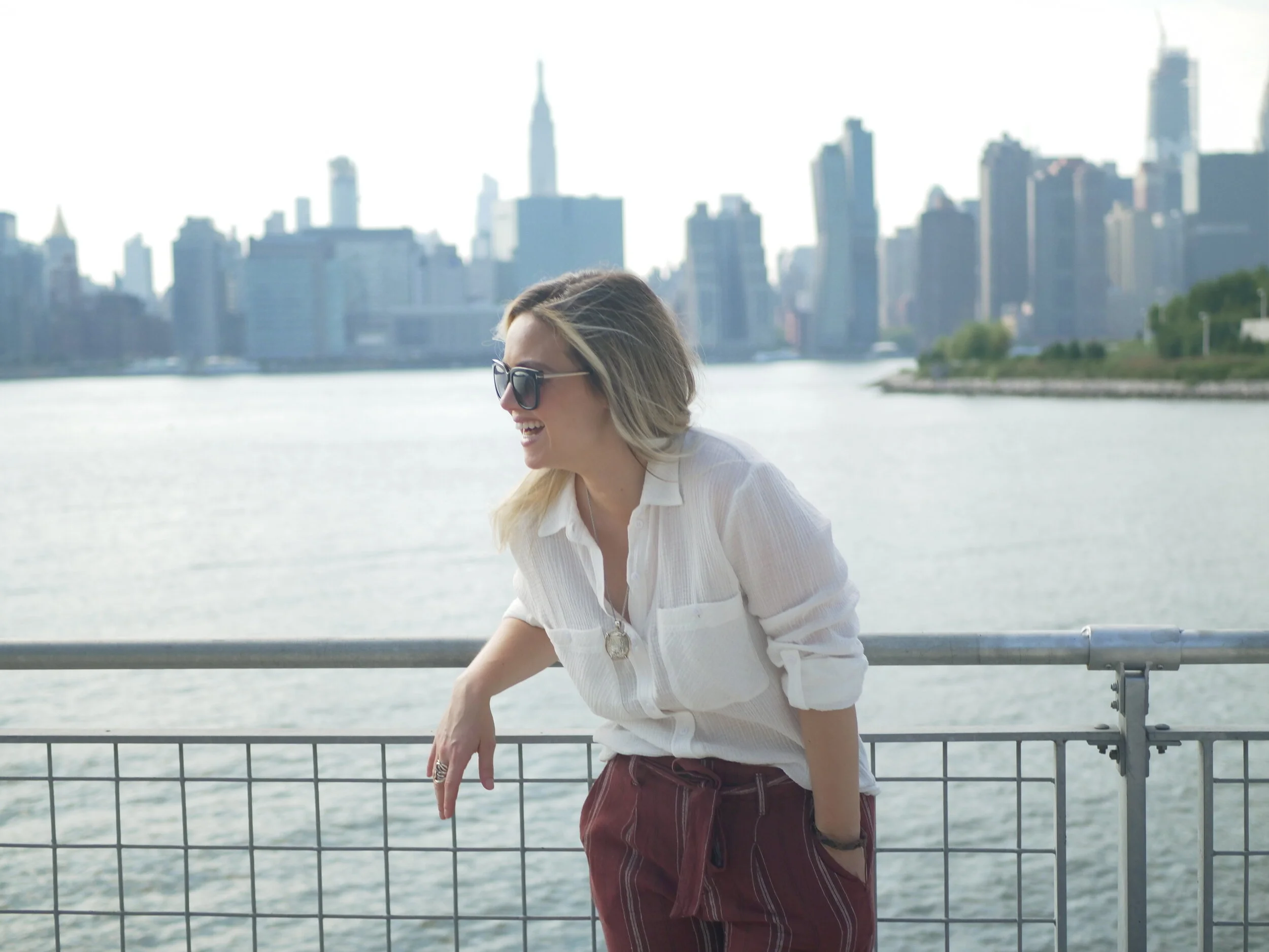 Alex leaning on a railing with the New York City skyline behind her