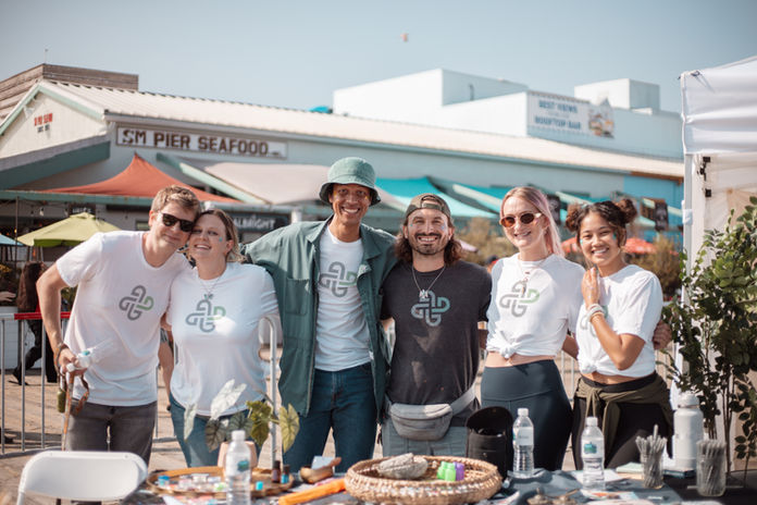 Group of six smiling people in branded t-shirts near Santa Monica Pier