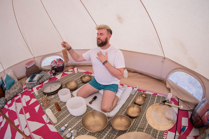 Man with singing bowls inside a bell tent in a meditative pose