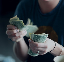 Person counting US dollar bills representing event funding and sponsorships