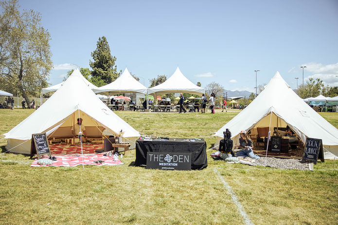 Two bell tents with The Den Meditation branded table at a sunny outdoor event
