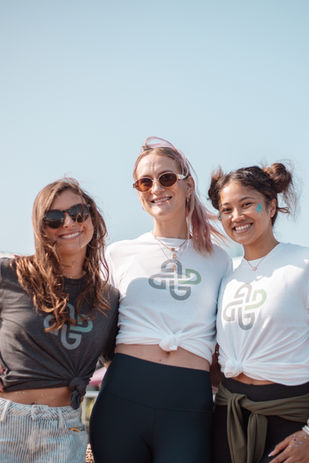 Three women smiling outdoors in branded t-shirts at a sunny event