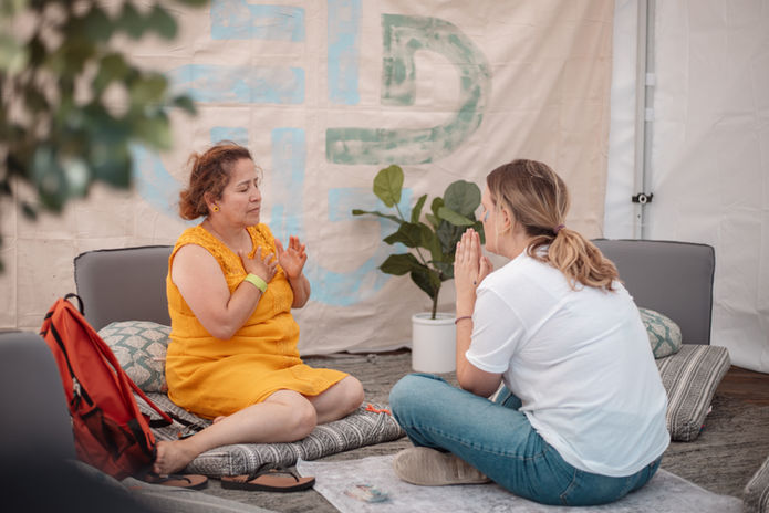 Two women meditating cross-legged facing each other inside a tent