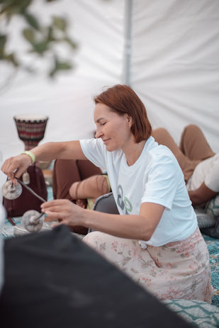 Red-haired woman in a branded t-shirt handling small bowls inside a tent