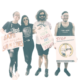 Four people standing together holding advocacy signs about drug-user rights and safe sites.