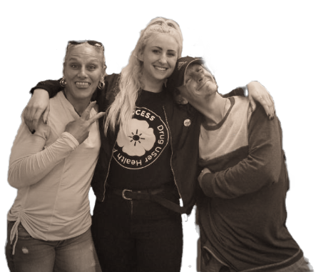 Sepia photo of three people posing together; the person in the center wears a Drug User Health Access t-shirt.